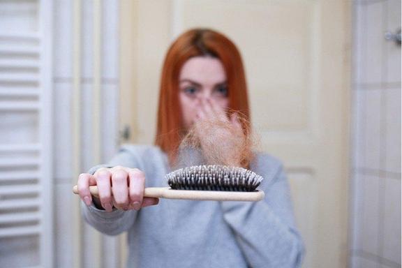 Frau mit roten Haaren hält erschrocken einen Kamm mit einem Haarbüschel in der Hand